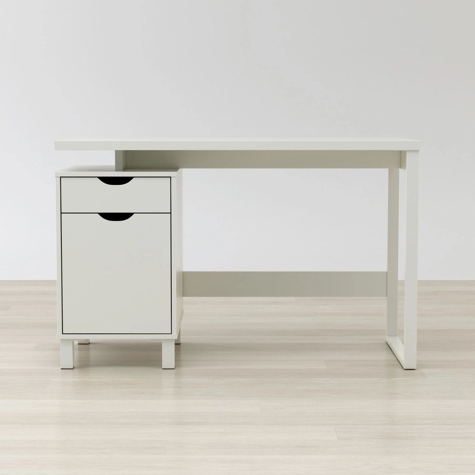 White desk with a small cabinet on a light wooden floor against a white wall