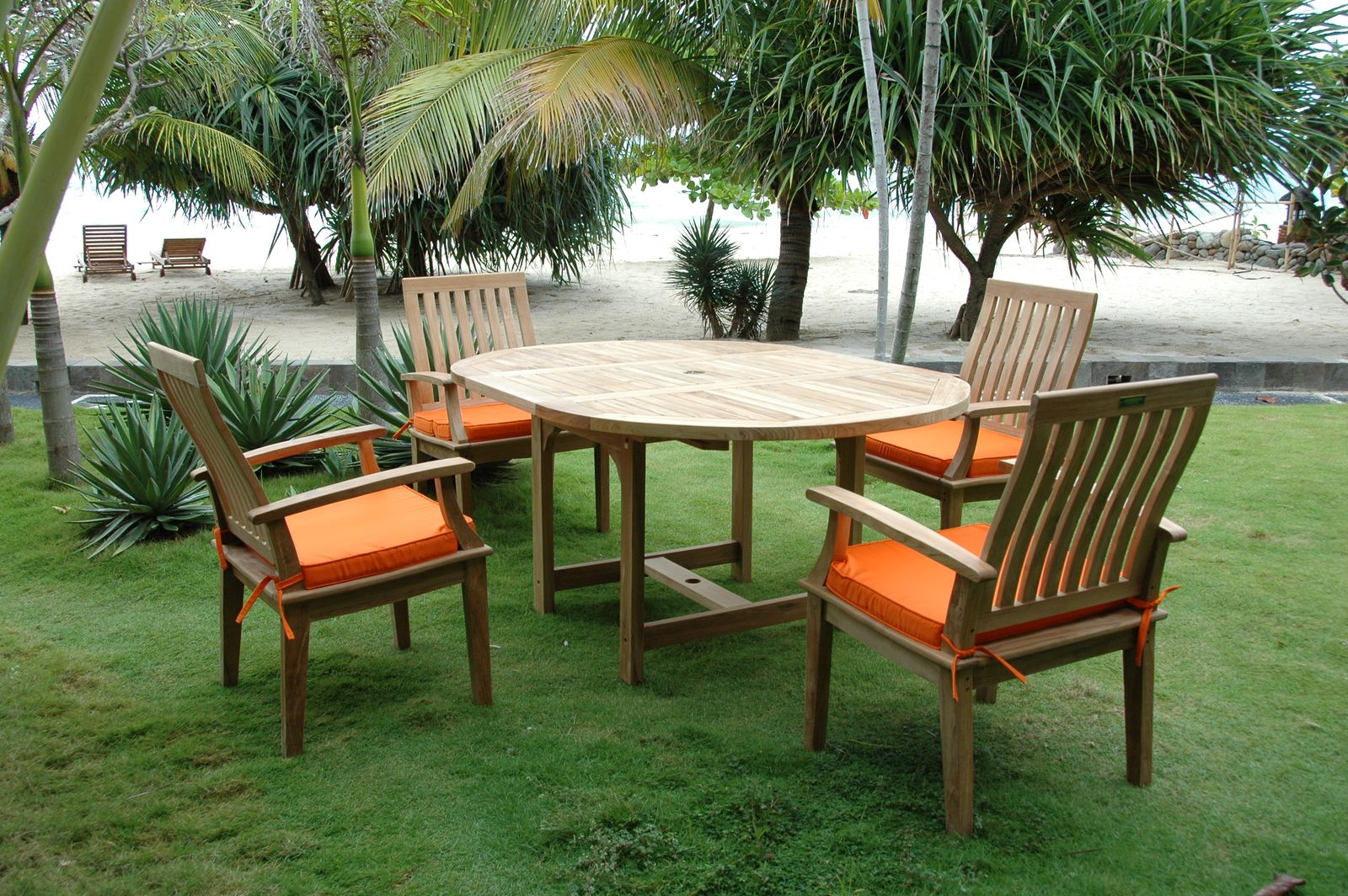 Outdoor wooden table with four matching chairs on a grassy area with palm trees in the background.