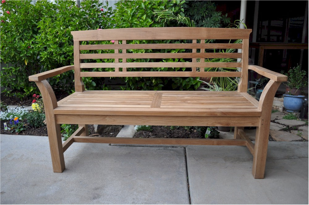 Wooden bench on a patio with greenery in the background