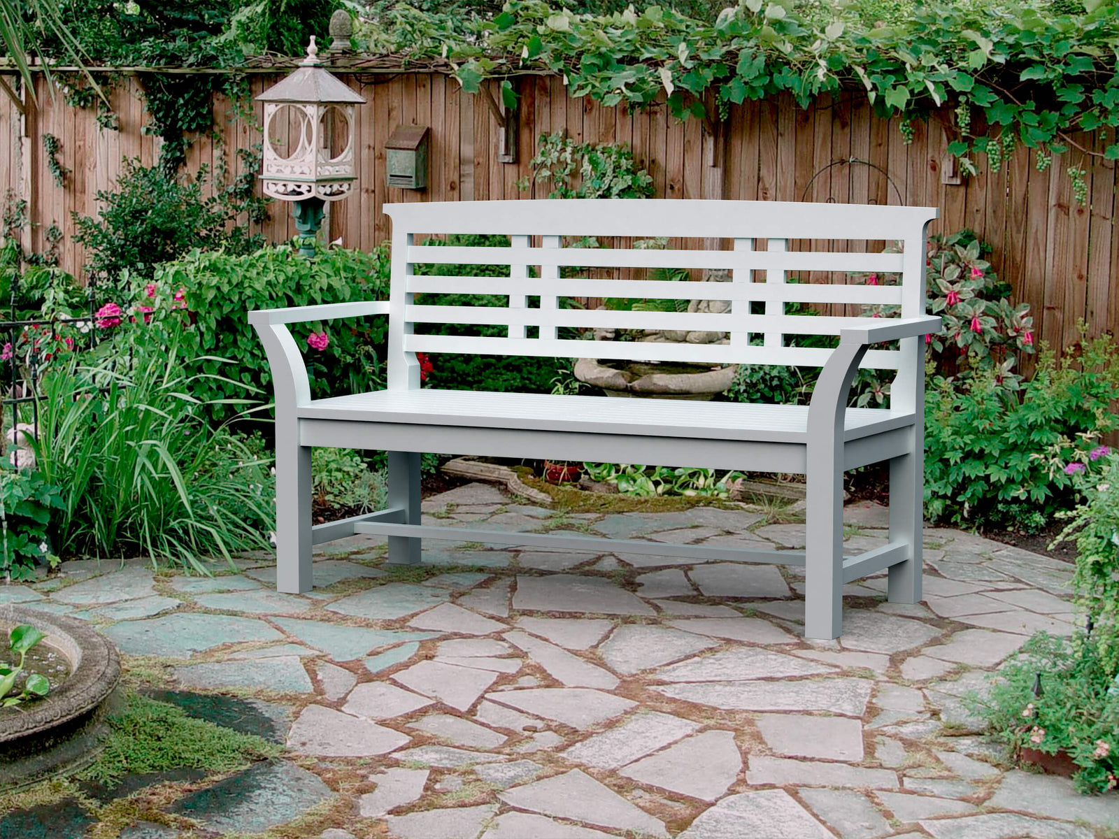 White bench on a stone patio with garden and wooden fence in the background