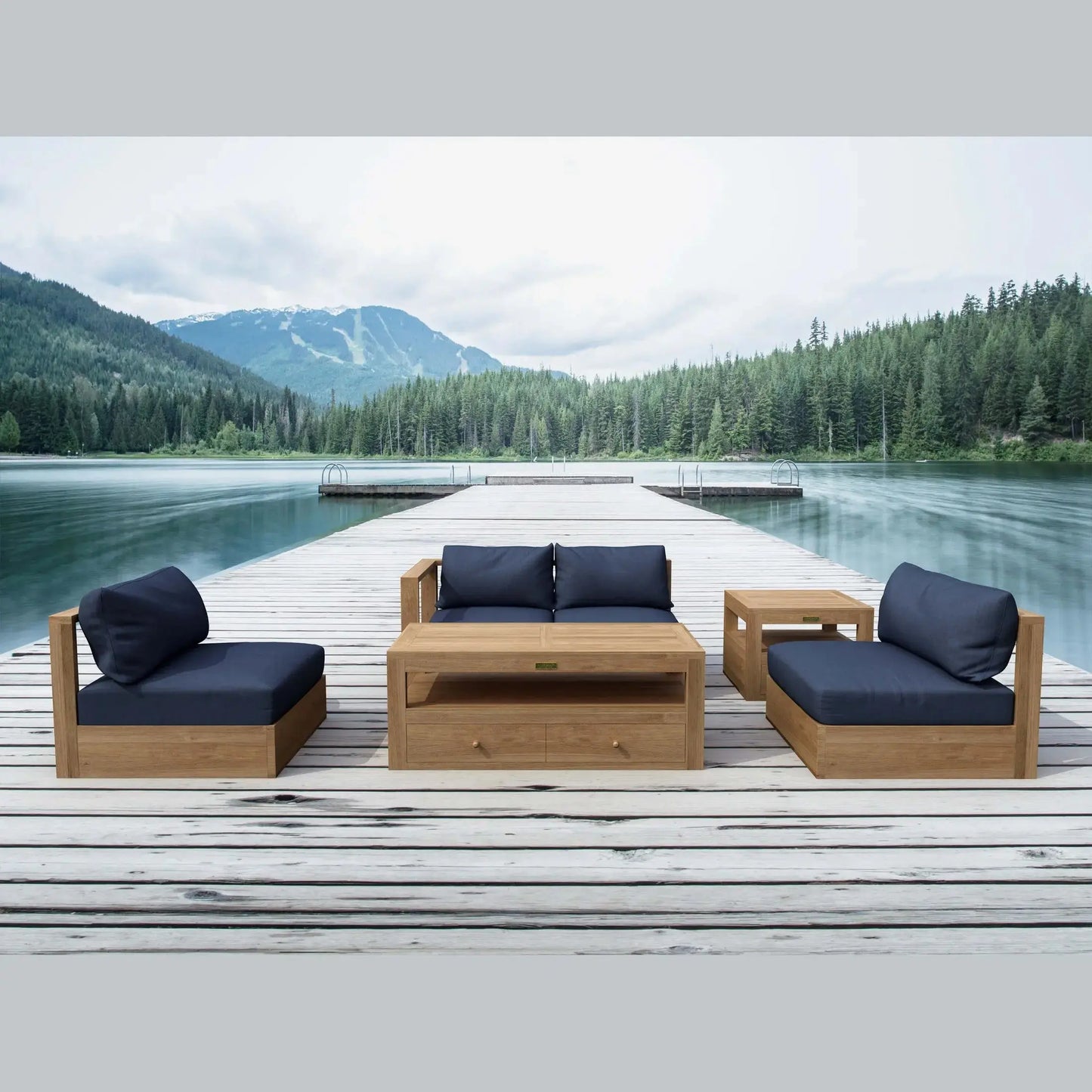 Outdoor wooden furniture set with blue cushions on a dock by a lake with mountains in the background