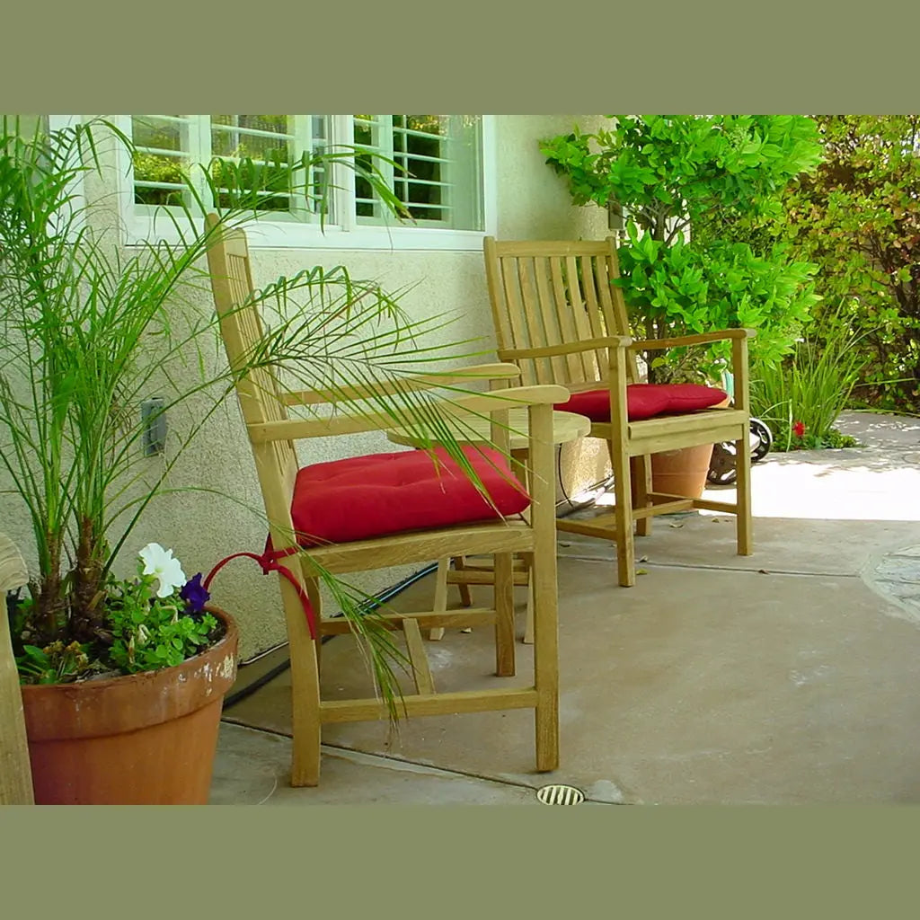 Two wooden chairs with red cushions on a patio, surrounded by plants.