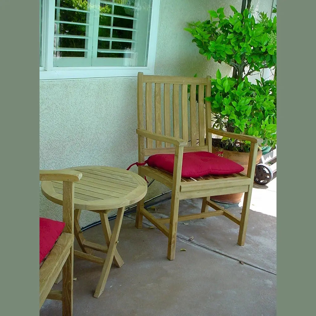Wooden chair with a red cushion on a patio next to a small round table.