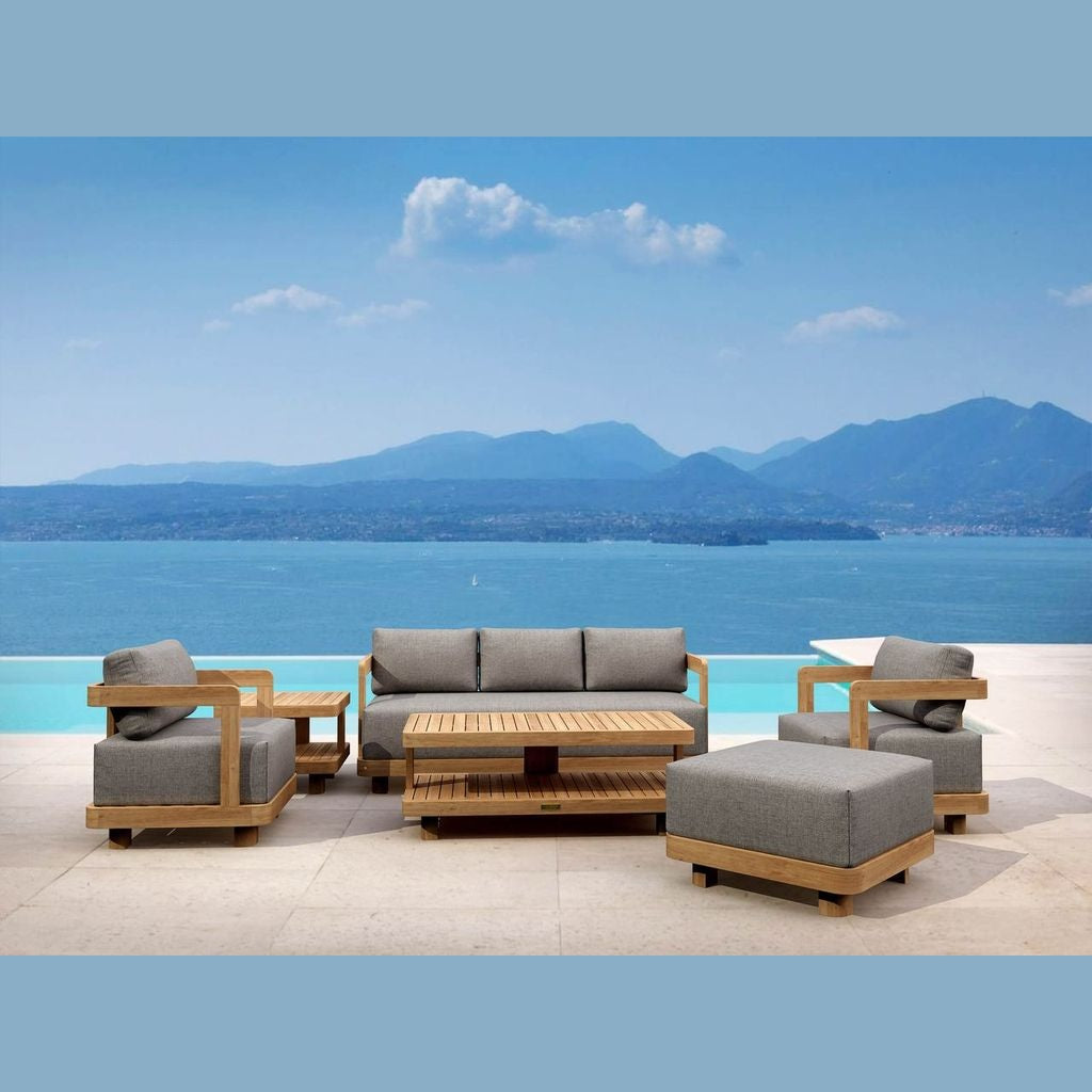 Outdoor furniture set with gray cushions and wooden frames by a scenic waterfront.