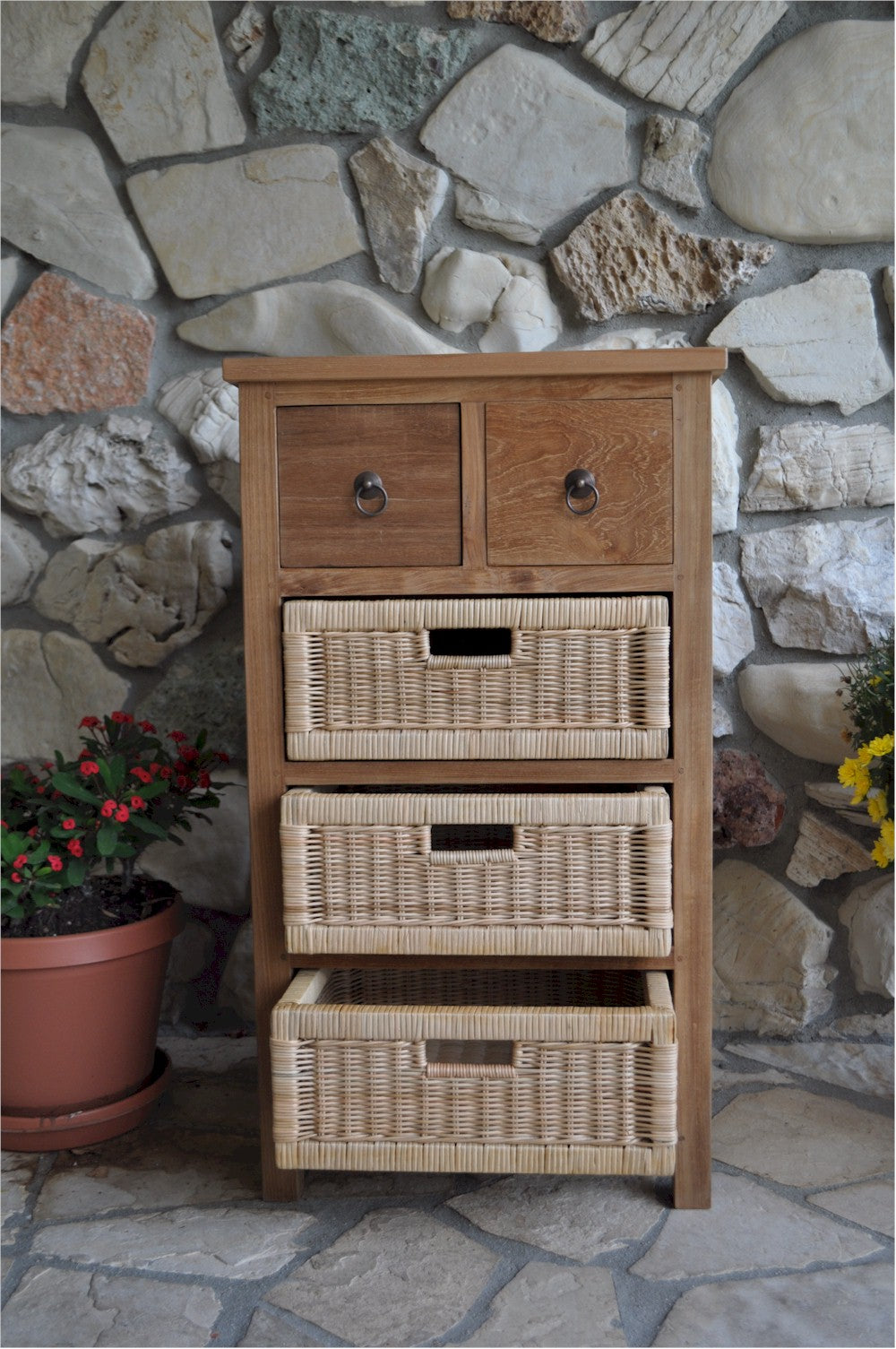 Wooden dresser with wicker drawers against a stone wall