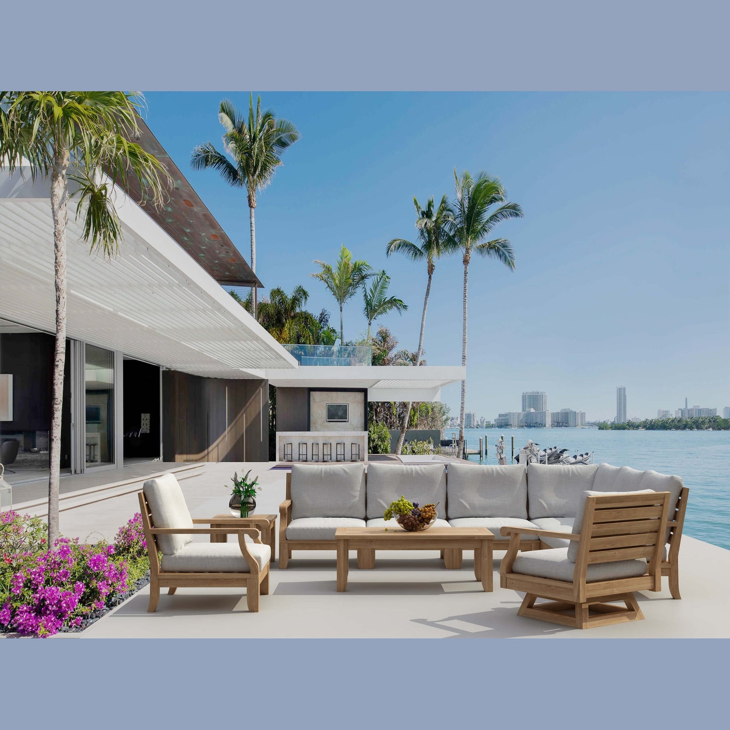Outdoor patio with furniture and palm trees by a waterfront.