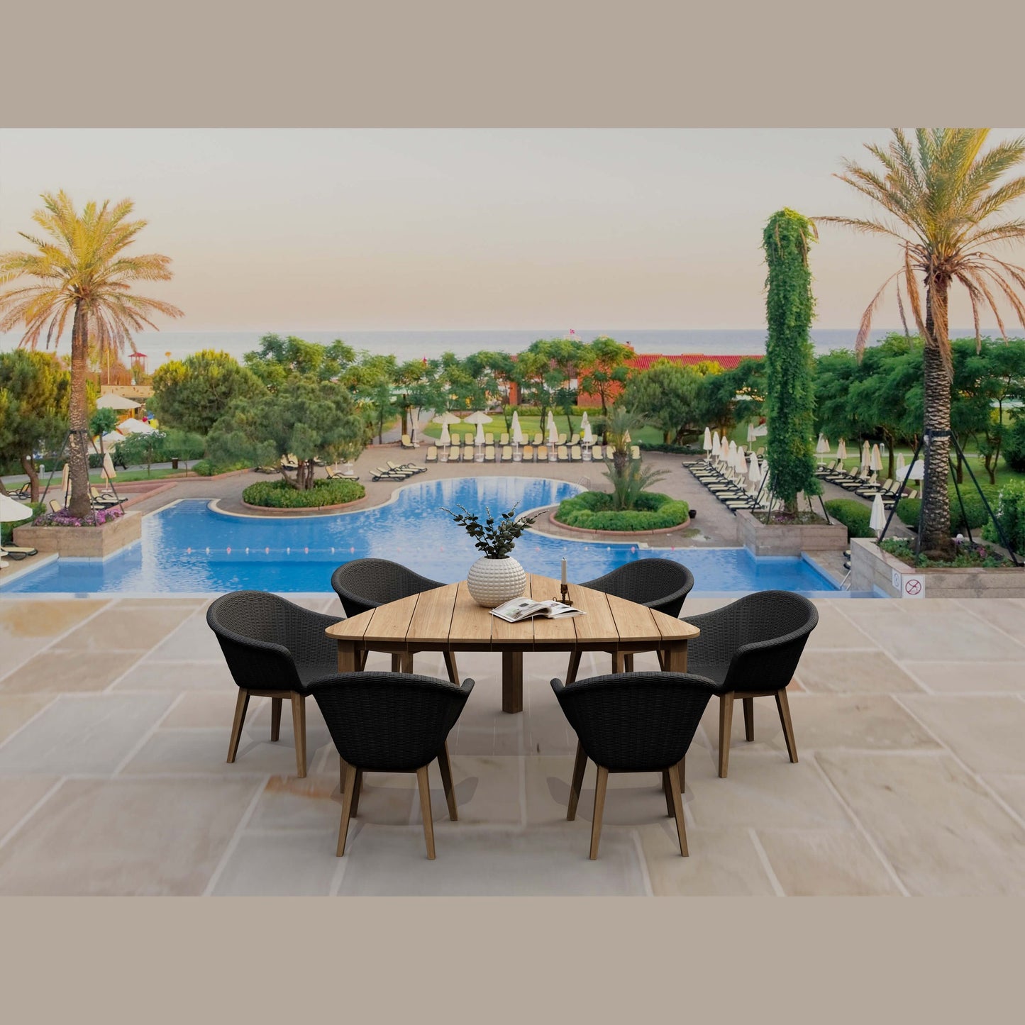 Outdoor dining area with a wooden table and black chairs near a pool with palm trees and greenery.