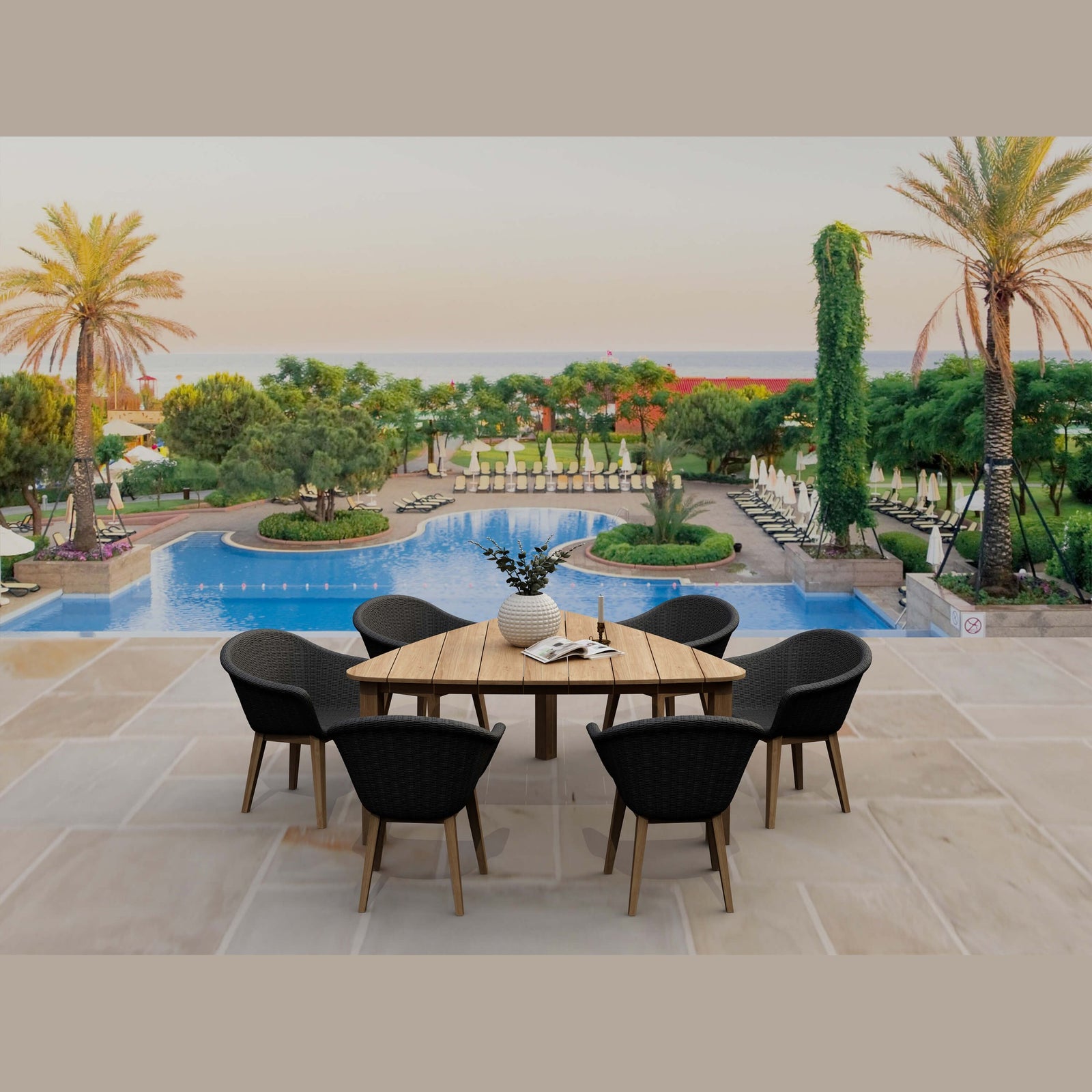 Outdoor dining area with a wooden table and black chairs near a pool with palm trees and greenery.