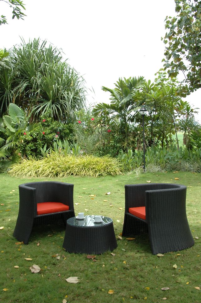 Outdoor furniture set with black chairs and a table on grass, surrounded by greenery.
