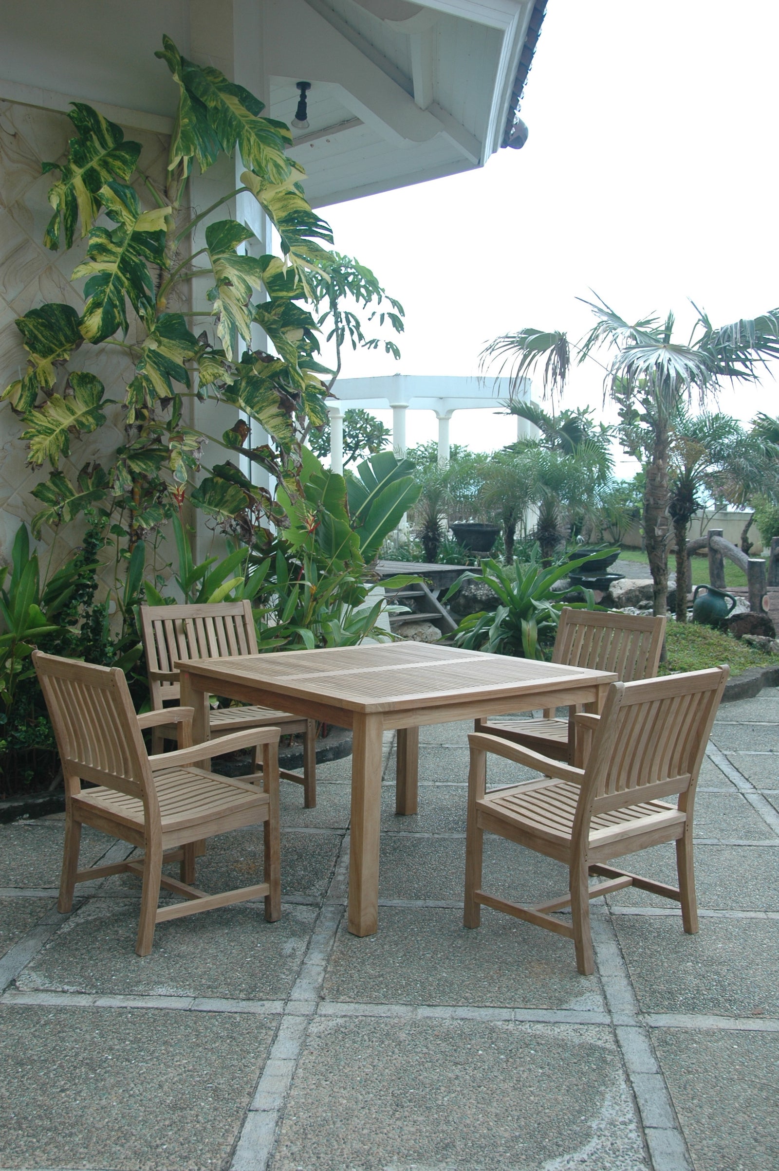 Wooden outdoor dining set with chairs on a patio surrounded by plants
