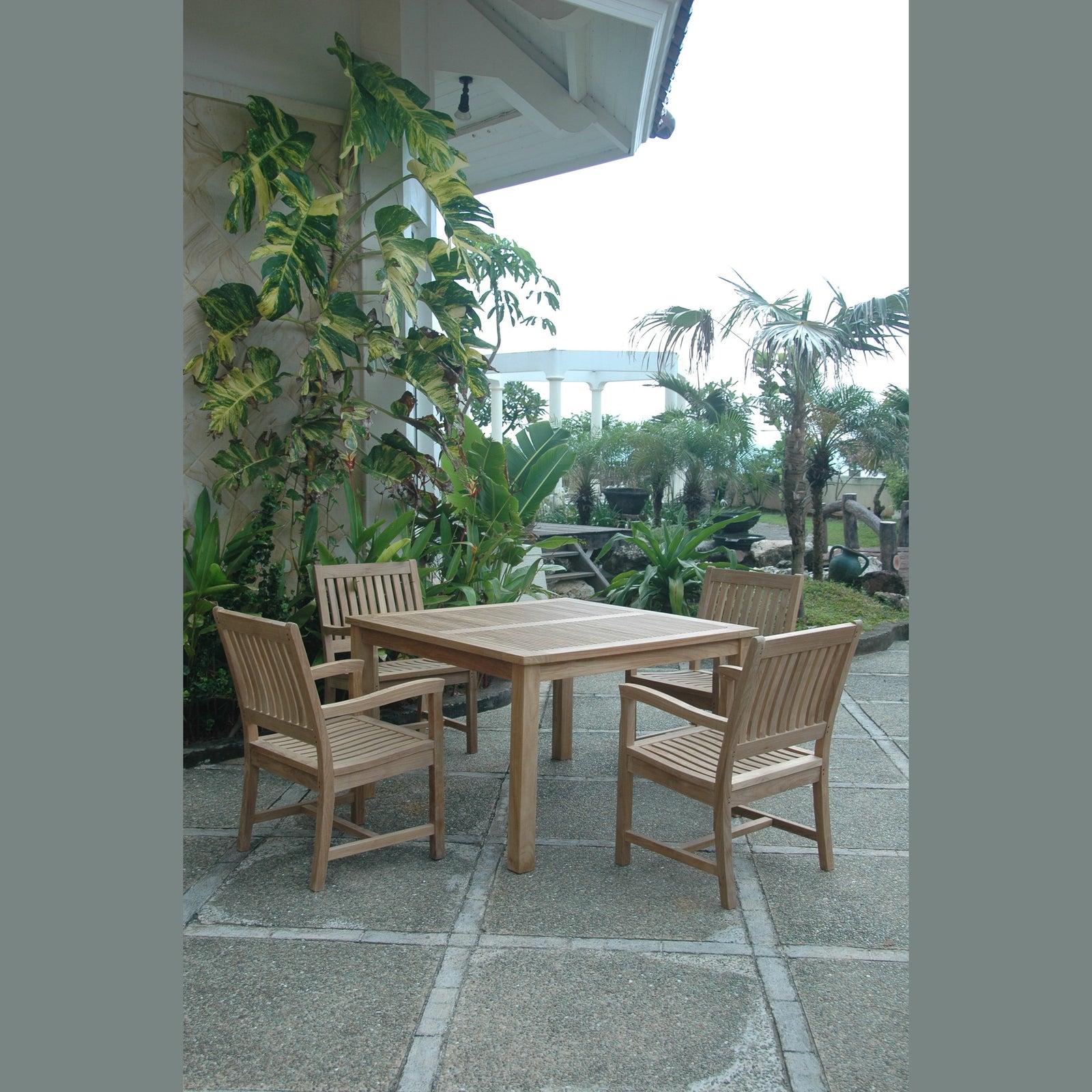 Wooden outdoor dining set with chairs on a patio surrounded by plants