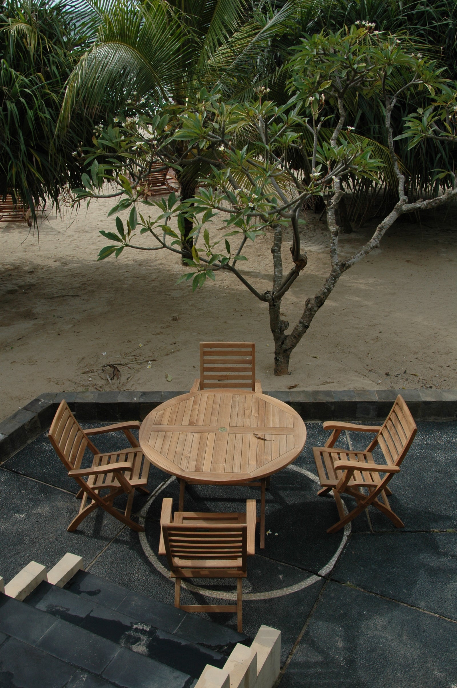 Wooden outdoor furniture set with a round table and chairs on a stone patio.