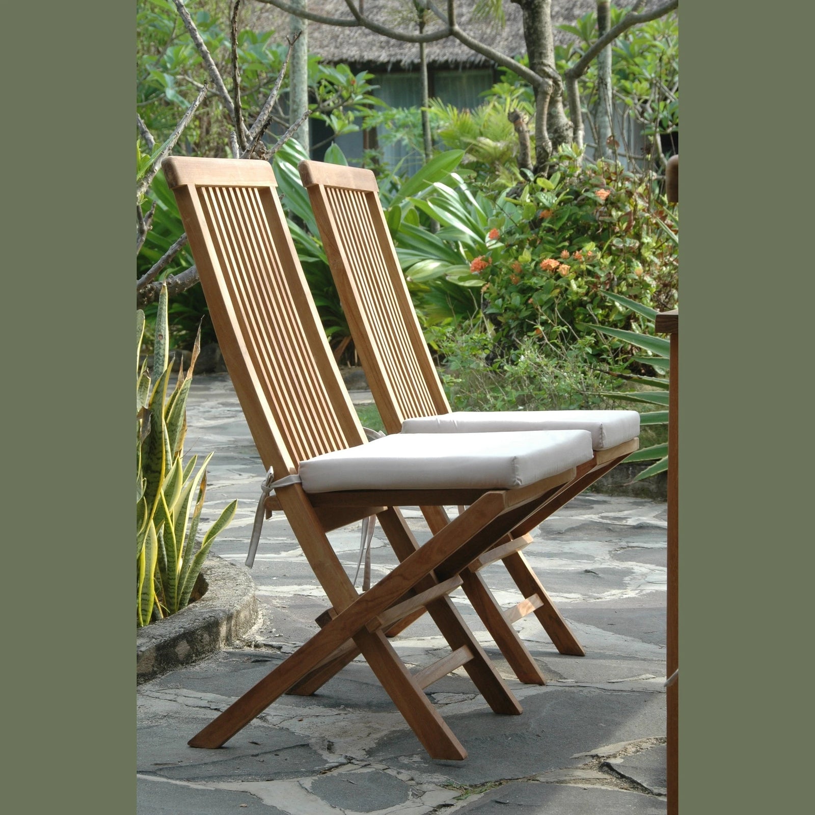 Two wooden folding chairs with white cushions on a stone patio surrounded by greenery.