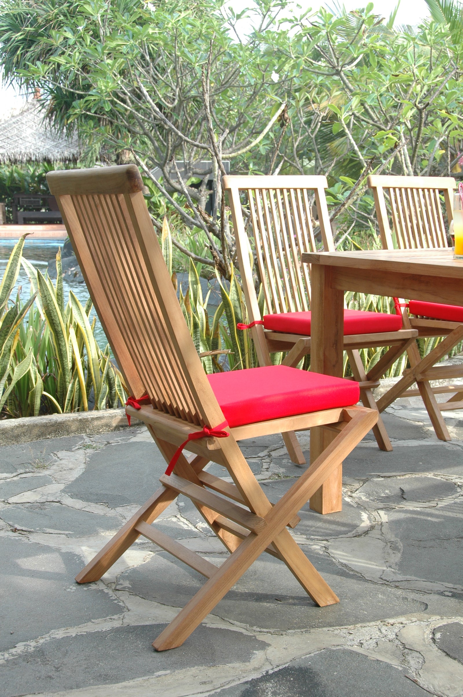 Wooden chairs with red cushions on a stone patio with a garden background
