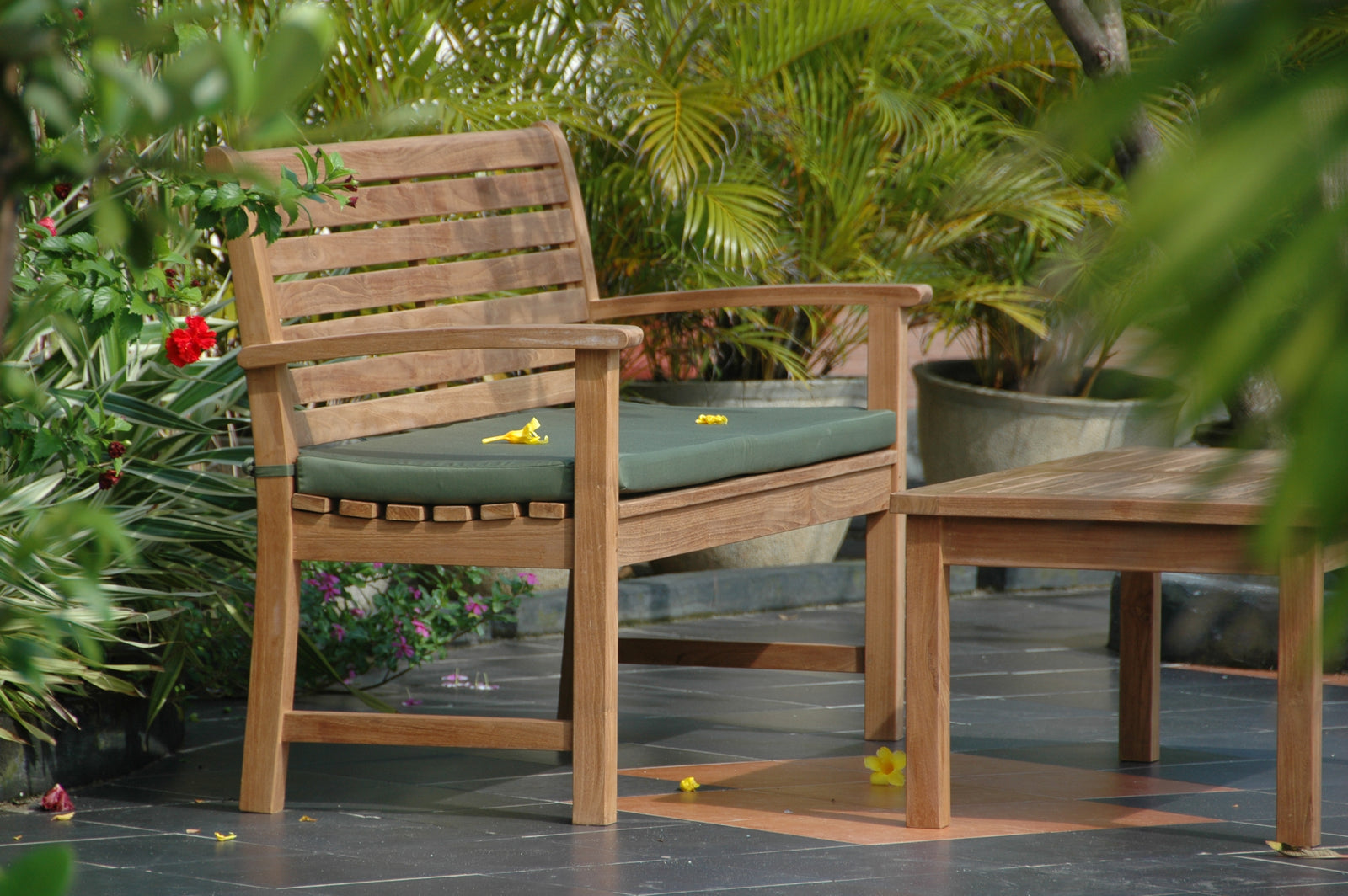 Wooden outdoor bench with green cushion on a patio surrounded by plants