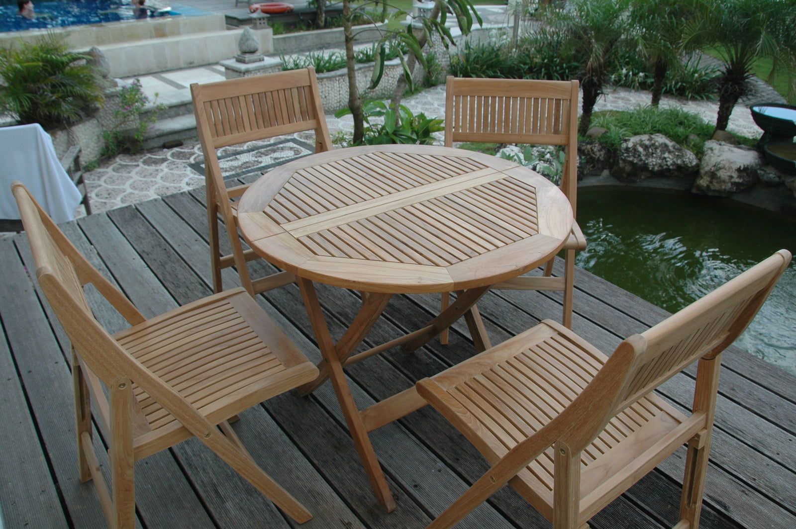 Wooden outdoor dining set with table and chairs on a wooden deck by a pond.
