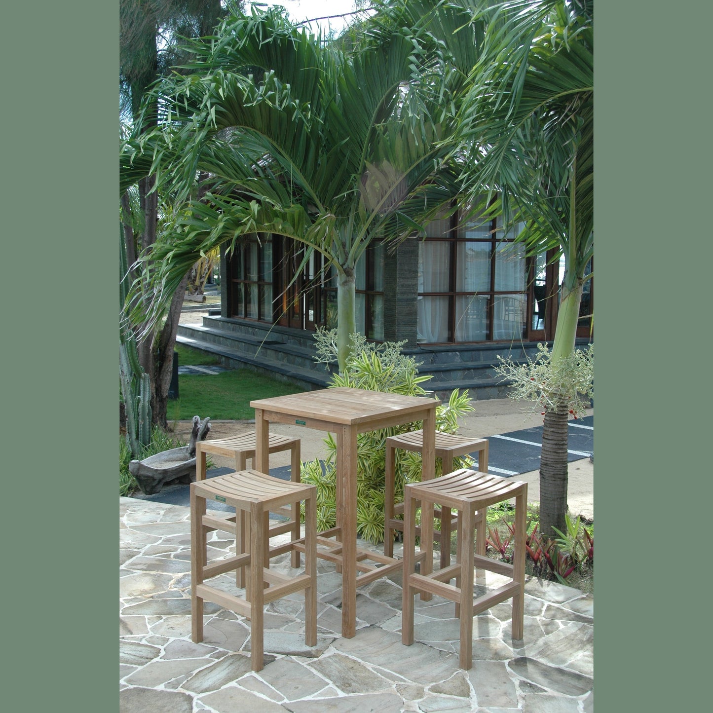 Outdoor setting with wooden table and stools surrounded by palm trees and a building in the background.