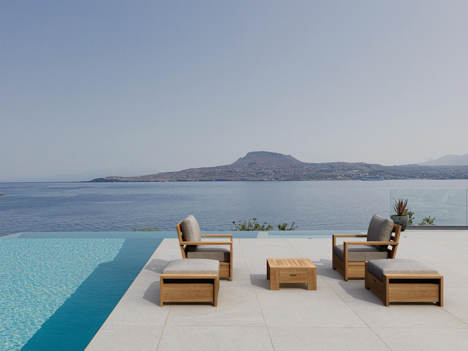 Wooden outdoor furniture set by a pool with a scenic view of mountains and water.
