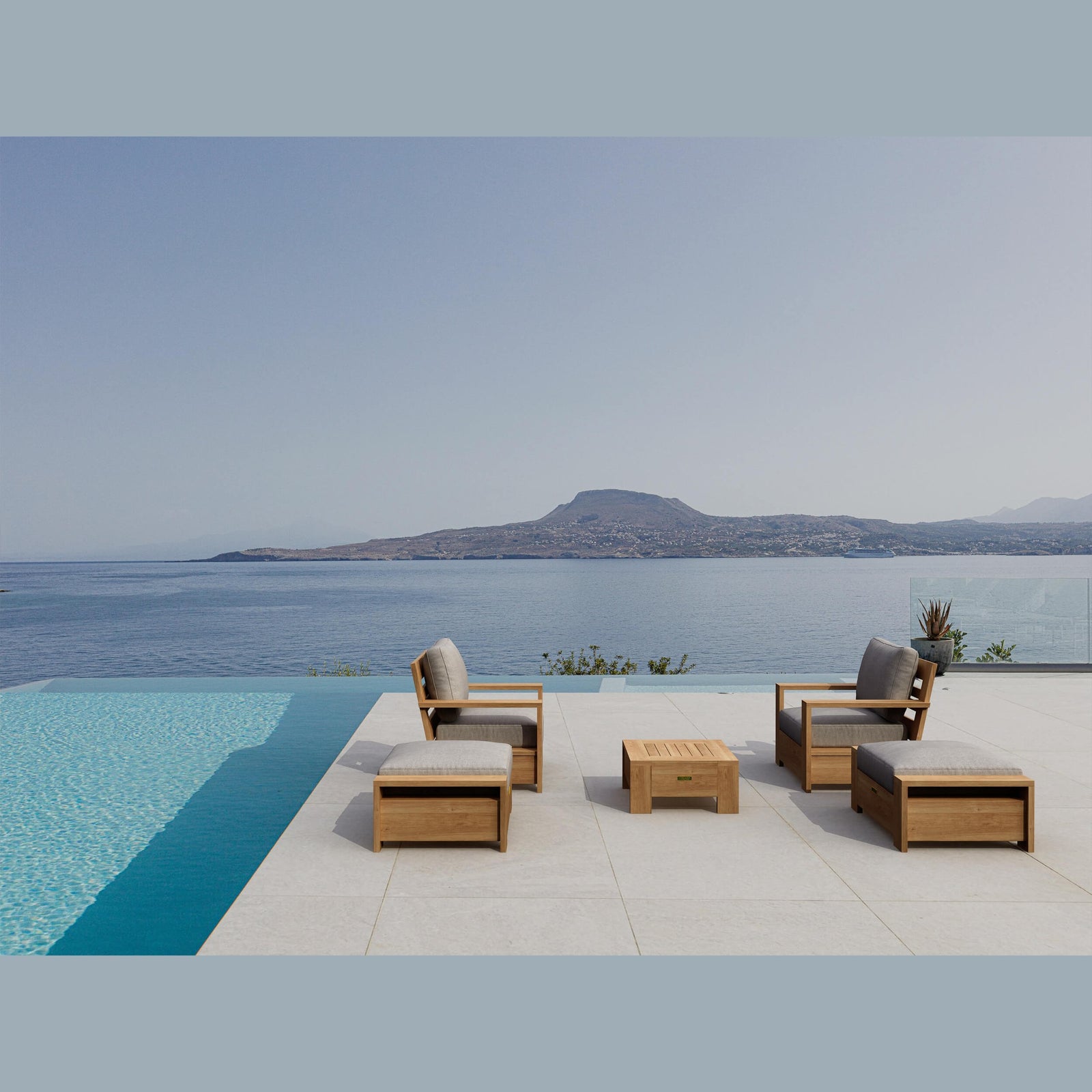 Wooden outdoor furniture set by a pool with a scenic view of mountains and water.