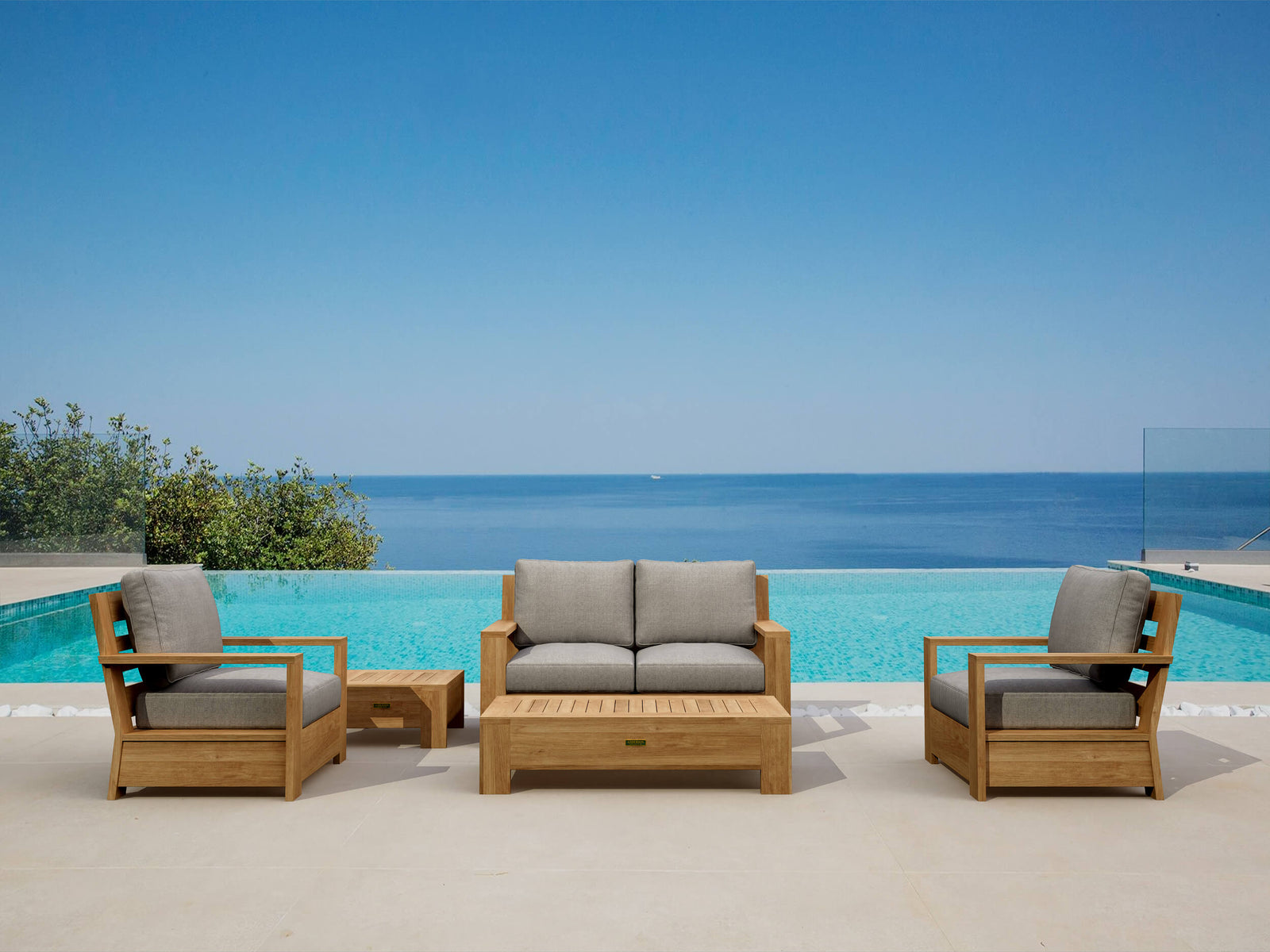 Outdoor wooden furniture set with gray cushions by a pool and blue sky.