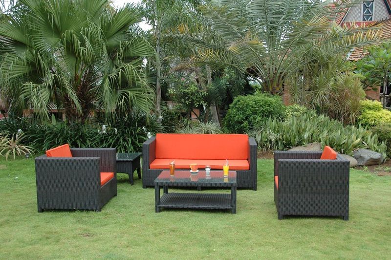 Outdoor furniture set with orange cushions on a grassy area with greenery.