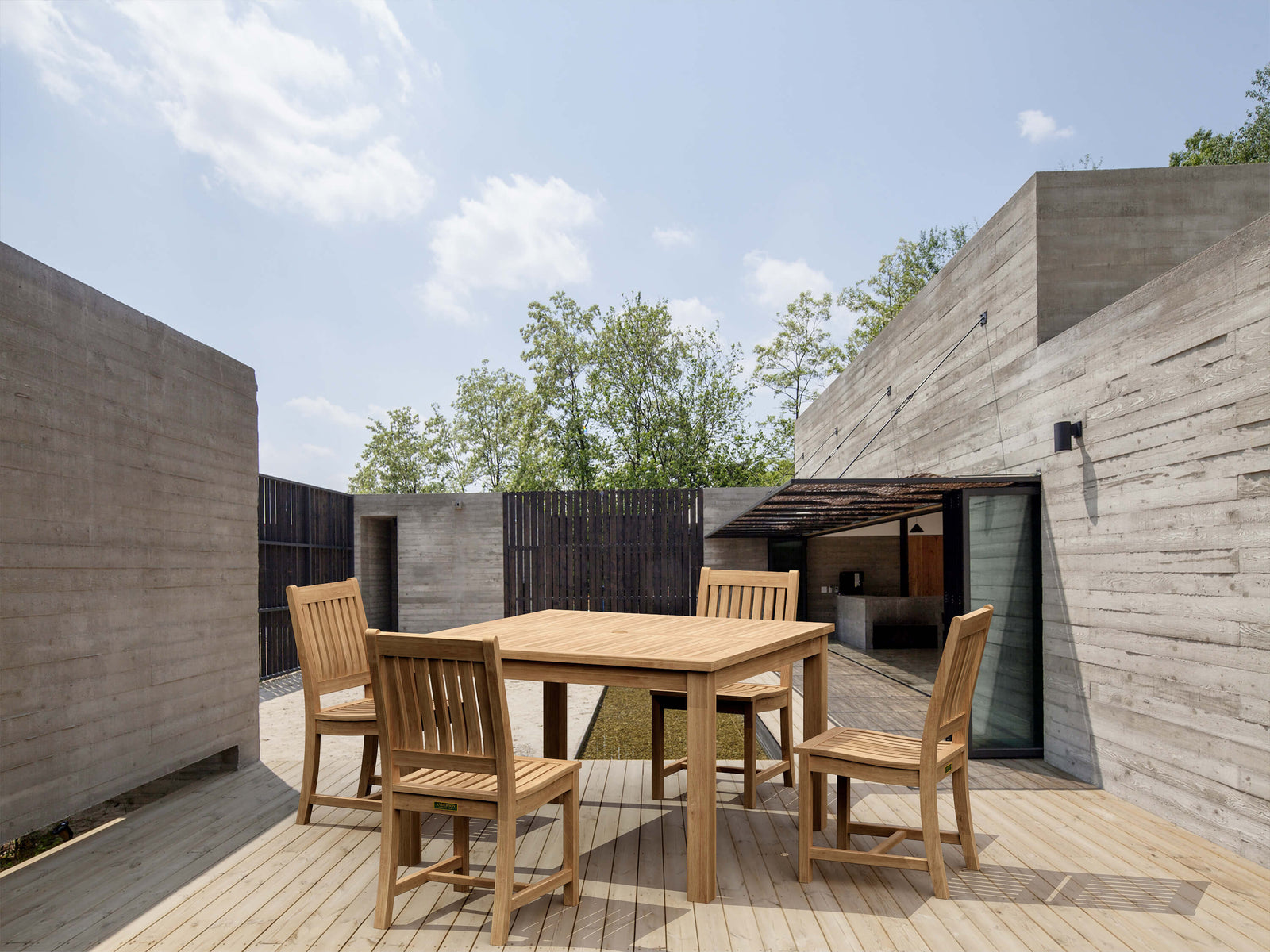 Wooden outdoor dining table with chairs in a modern architectural setting.