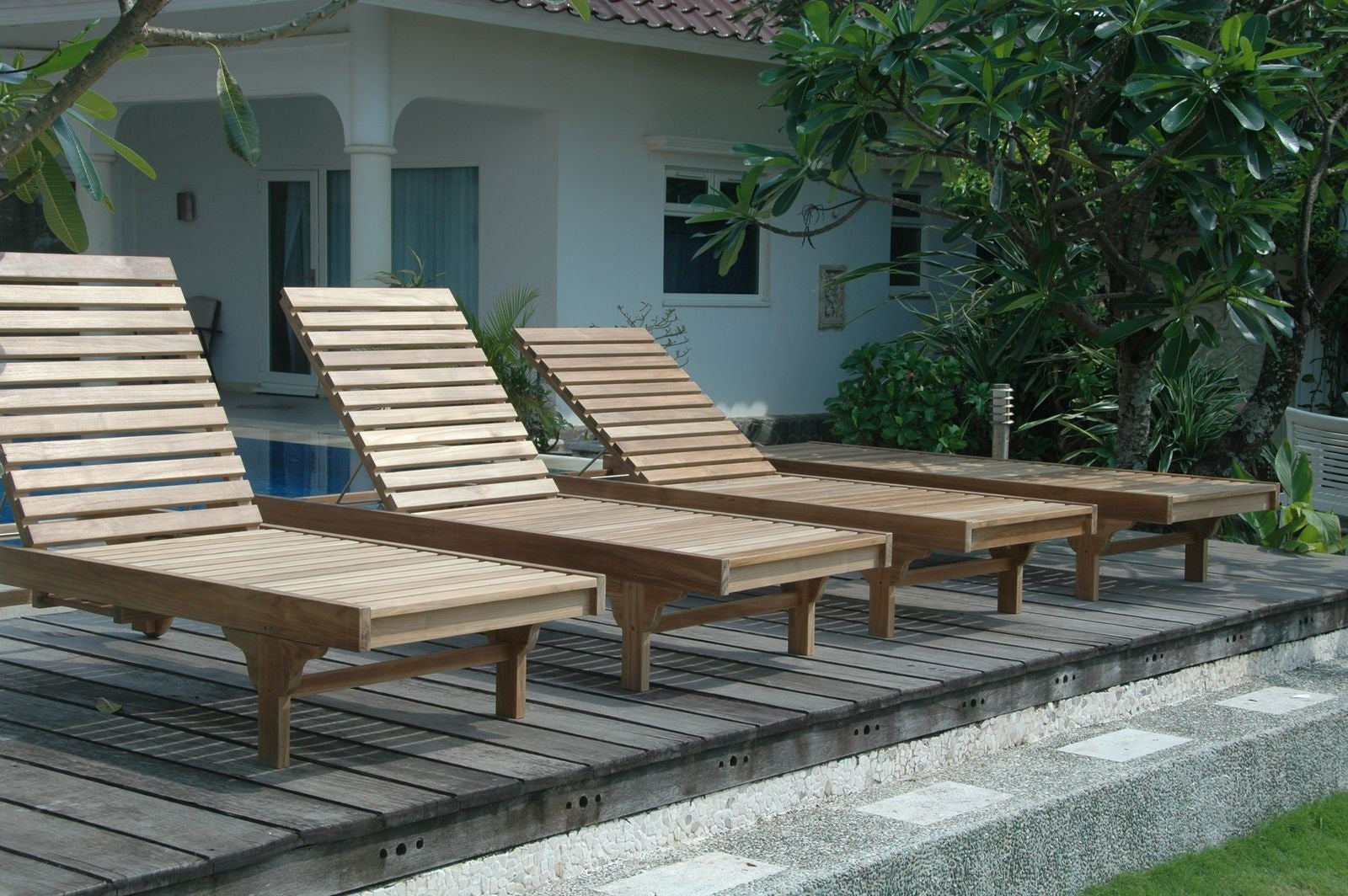 Wooden lounge chairs on a wooden deck with a building and greenery in the background