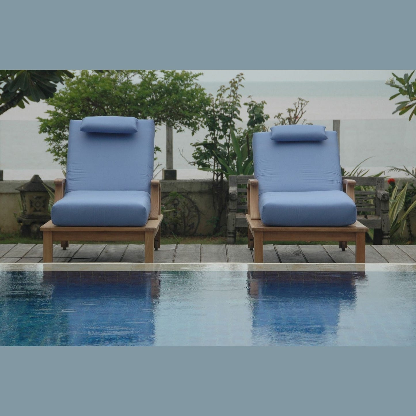 Two blue cushioned chairs by a poolside with a garden background