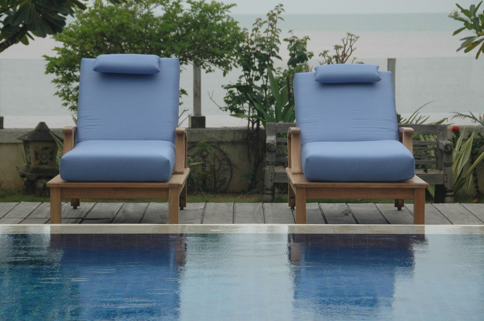 Two blue cushioned chairs by a poolside with a garden background