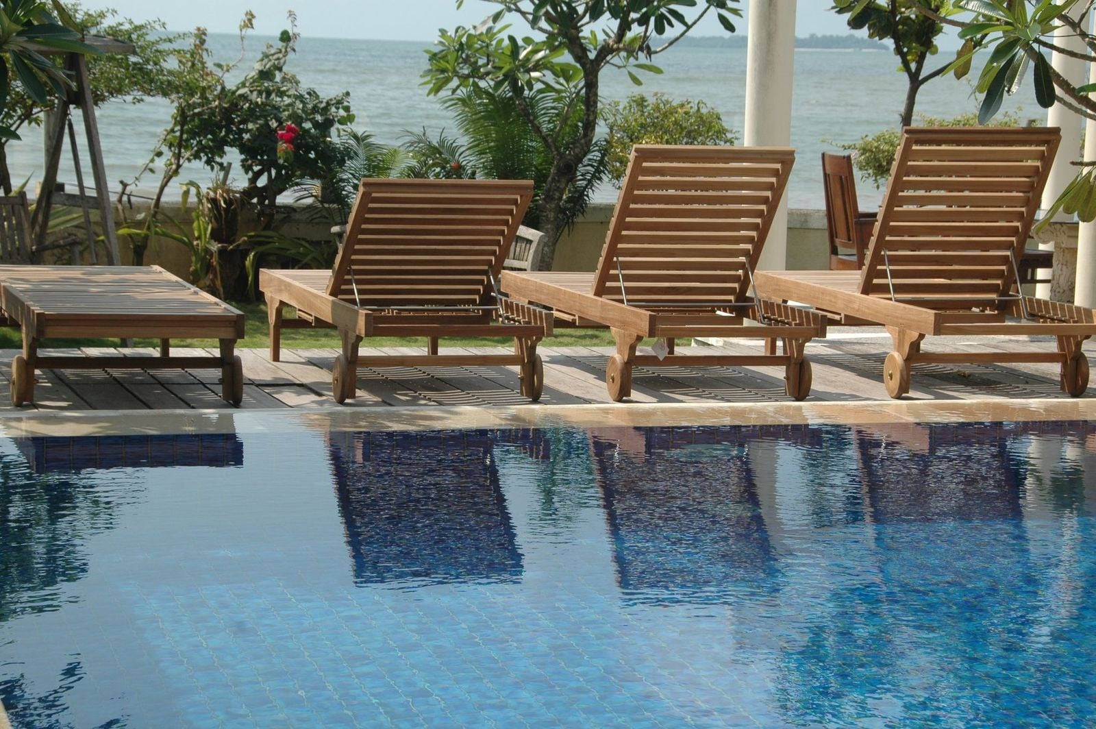 Wooden lounge chairs by a pool with a scenic view of water and trees.