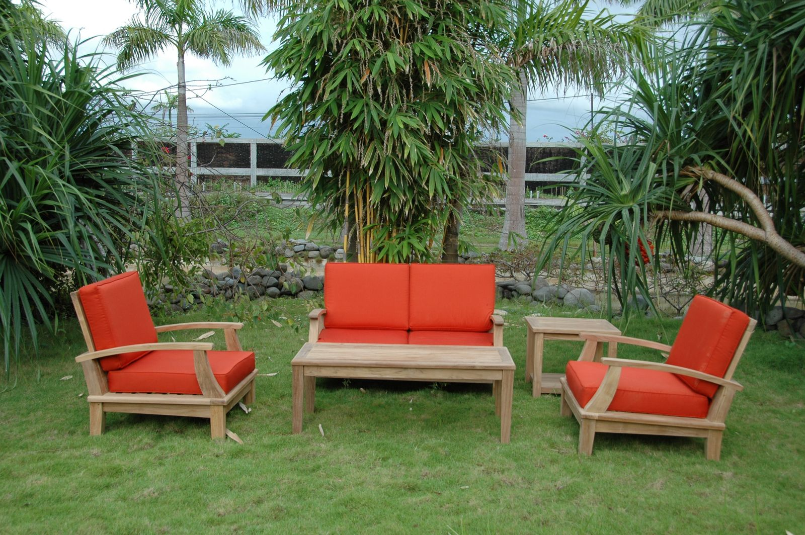 Outdoor furniture set with red cushions on a grassy area with trees in the background