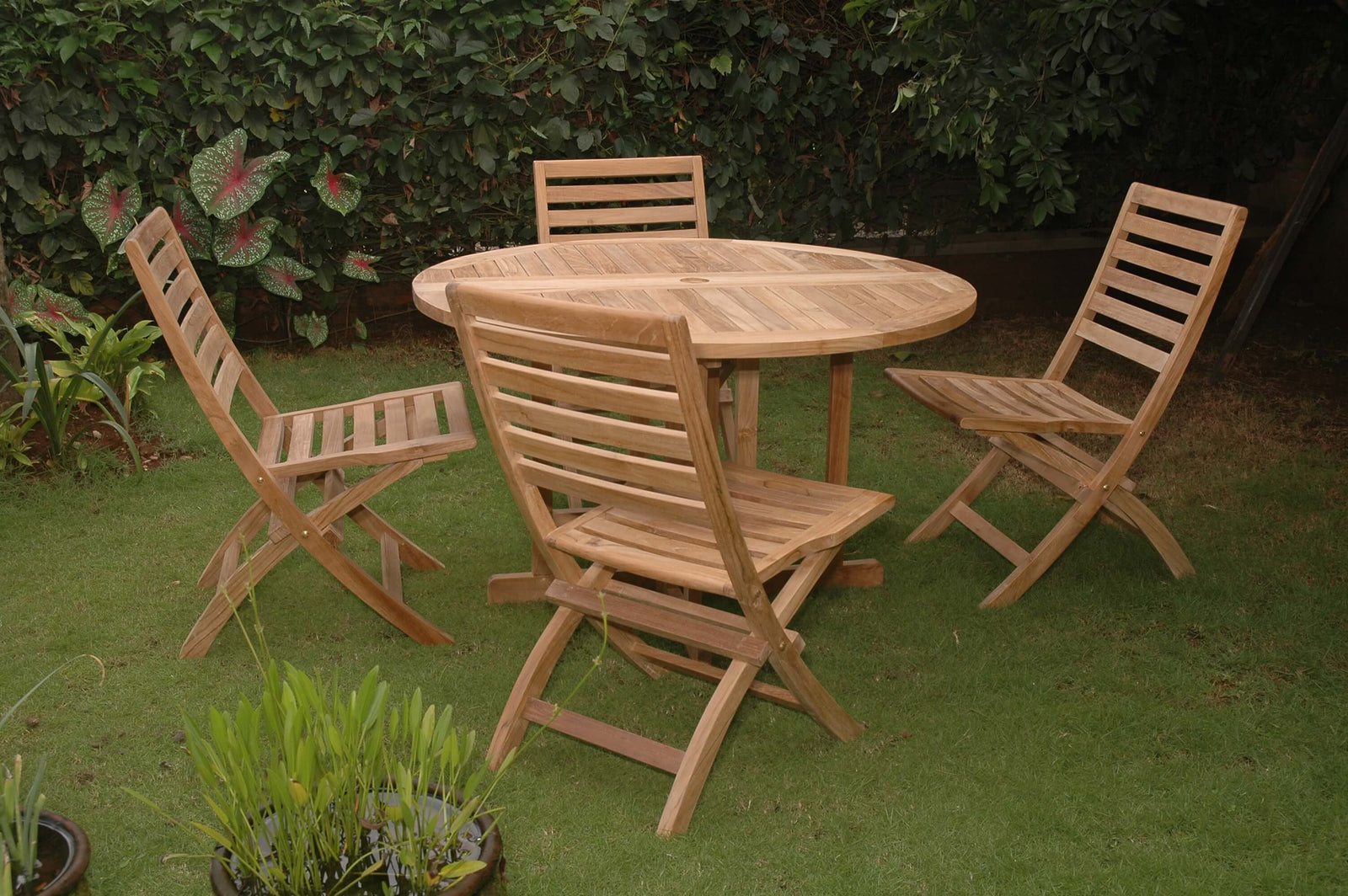 Wooden outdoor dining set with round table and four chairs on a grassy area.