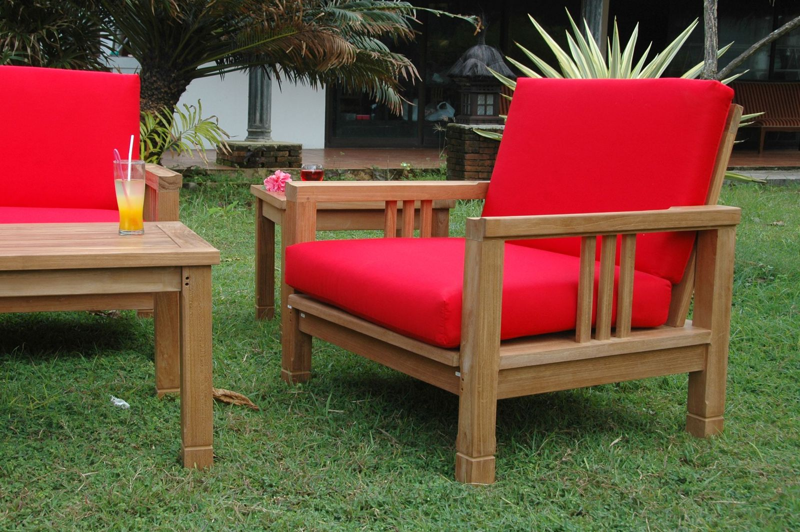Wooden outdoor furniture set with red cushions on a grassy area.