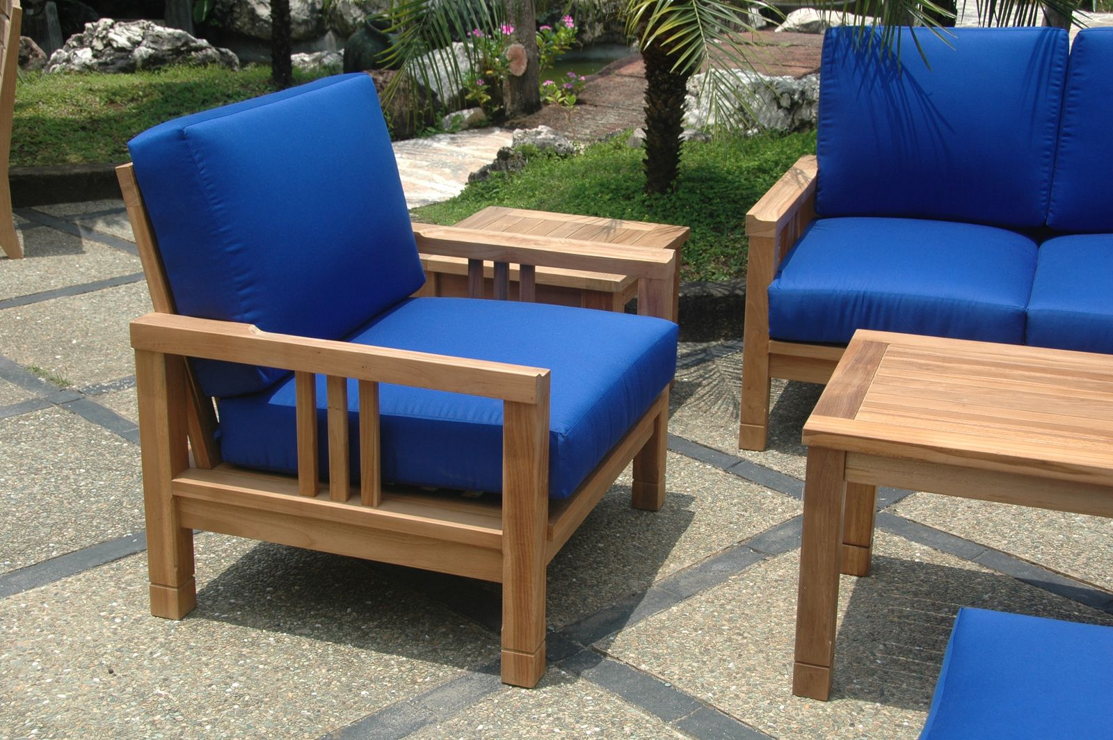 Wooden outdoor furniture set with blue cushions on a stone patio.