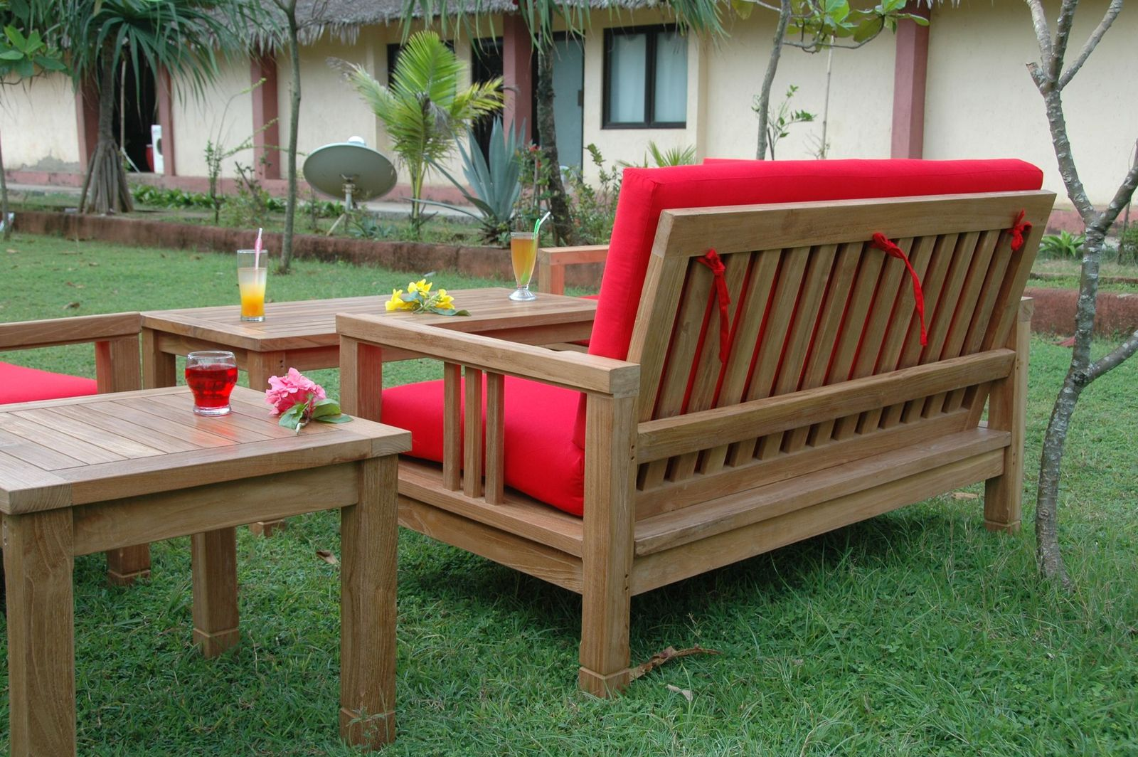 Wooden outdoor furniture set with red cushions on a grassy area.