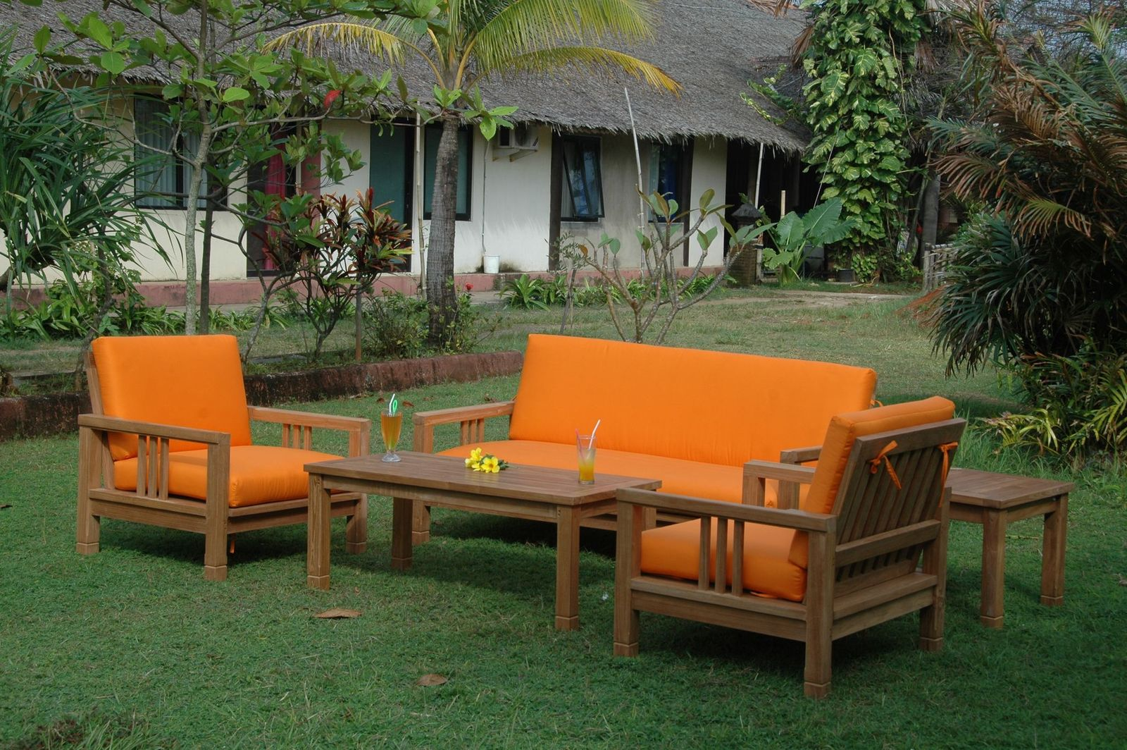 Outdoor furniture set with orange cushions on a grassy area with a building in the background.