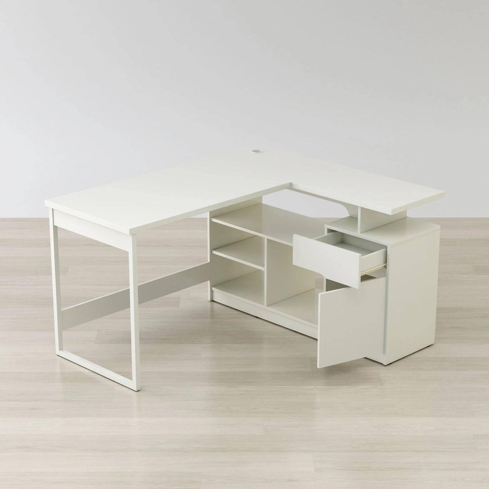 White L-shaped desk with a drawer on a light wooden floor.