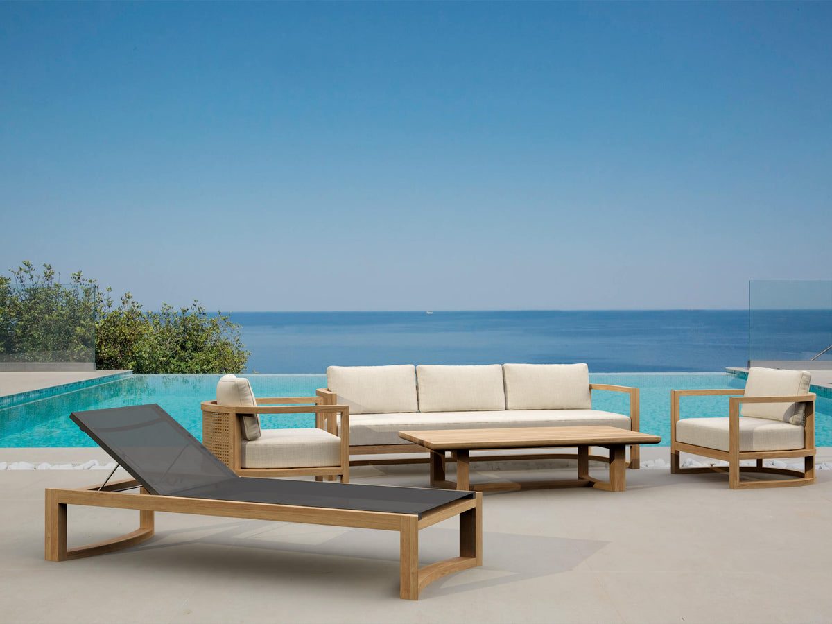 Outdoor furniture set with lounge chair, sofa, and table by a pool with ocean view.