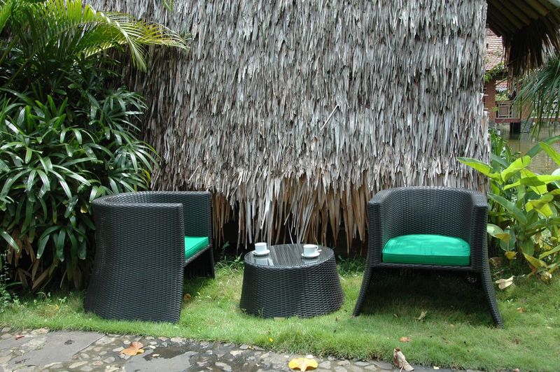 Outdoor furniture set with black chairs and table against a thatched wall.
