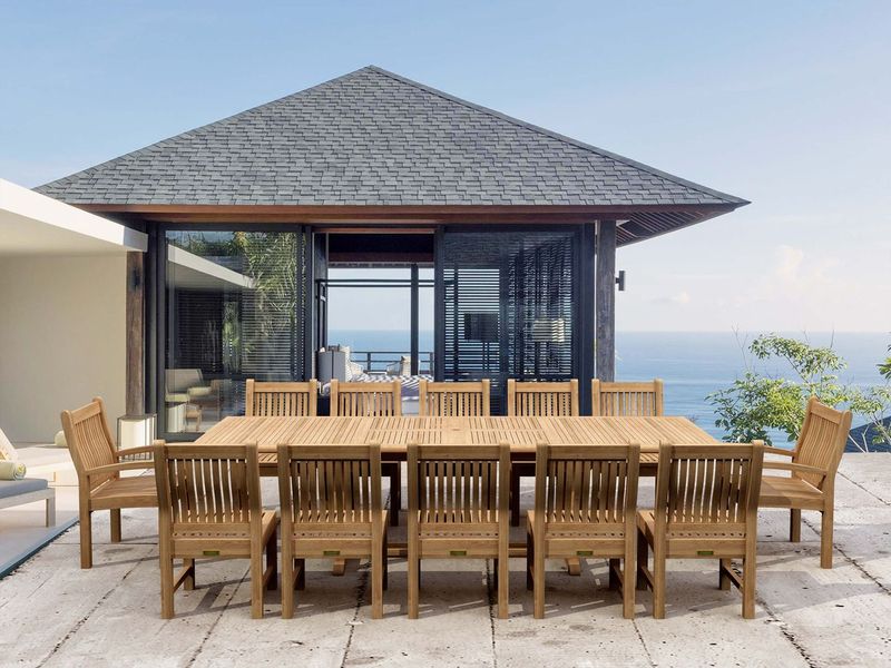 Wooden outdoor dining set with chairs on a patio area with a house and ocean view.