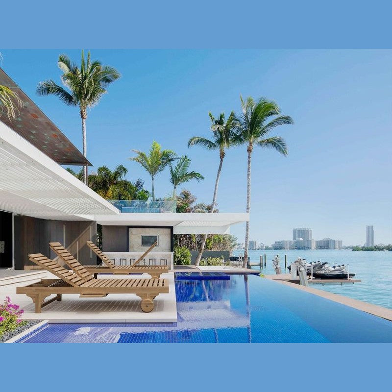 Modern house with a pool and lounge chairs by the water, palm trees in the background