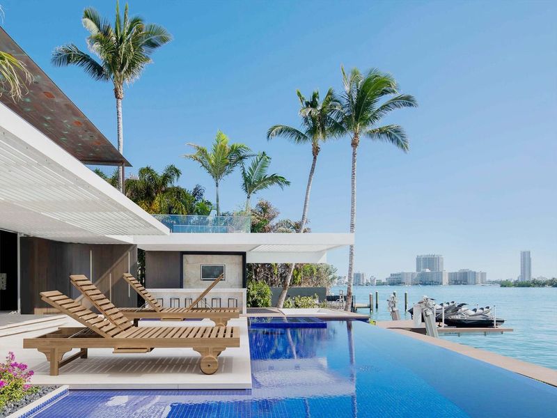 Modern house with a pool and lounge chairs by the water, palm trees in the background