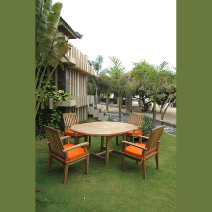 Outdoor wooden table with orange cushions surrounded by chairs on a grassy area with a building and trees in the background.
