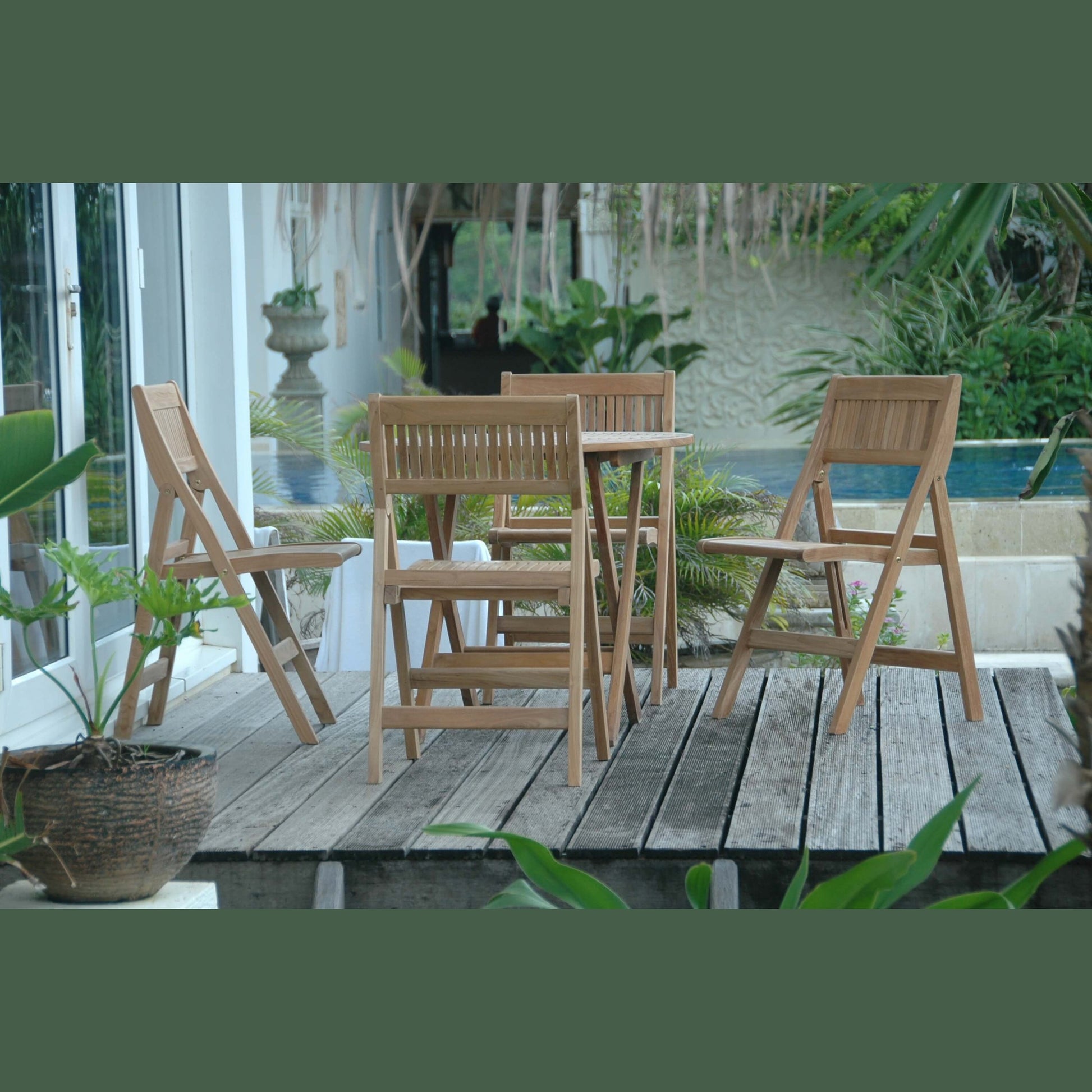 Wooden outdoor furniture set on a wooden deck with plants and a pool in the background