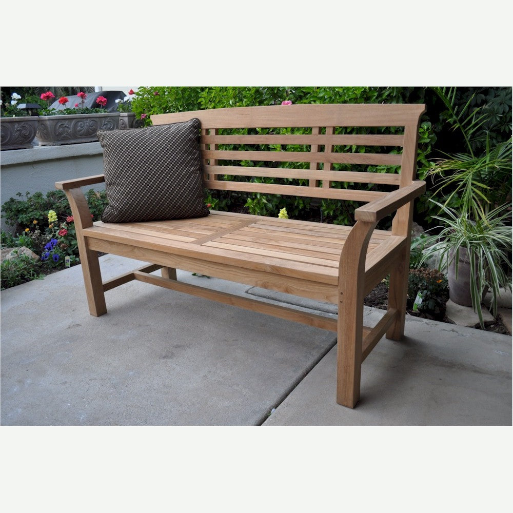 Wooden bench with a cushion on a patio area with plants and flowers in the background