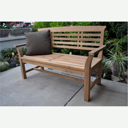 Wooden bench with a cushion on a patio area with plants and flowers in the background
