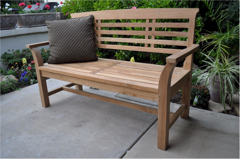 Wooden bench with a cushion on a patio area with plants and flowers in the background