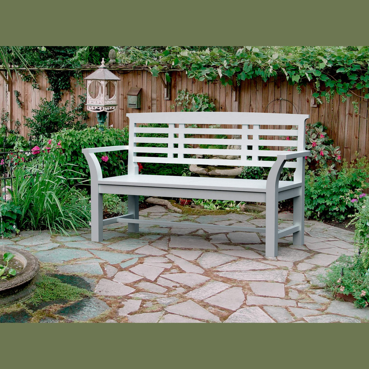 White bench on a stone patio with garden and wooden fence in the background