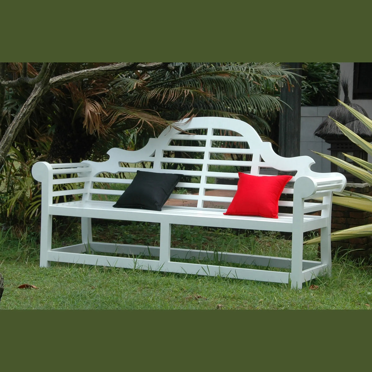 White garden bench with black and red cushions in a garden setting