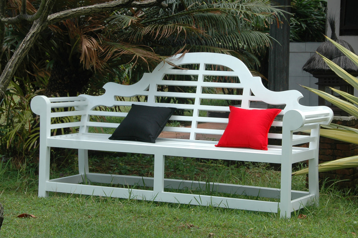 White garden bench with black and red cushions in a garden setting
